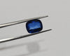 Blue gemstone held by tweezers on a gray background