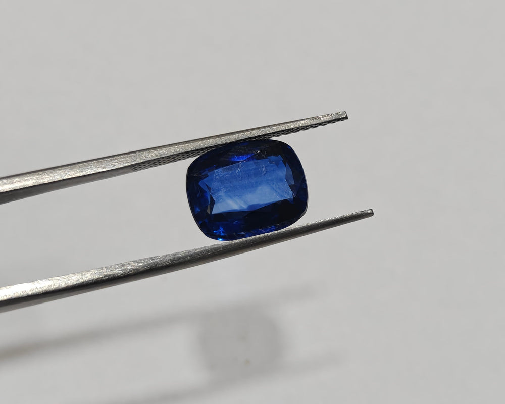 Blue gemstone held by tweezers on a gray background