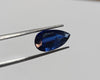 Blue gemstone held by tweezers on a light gray background