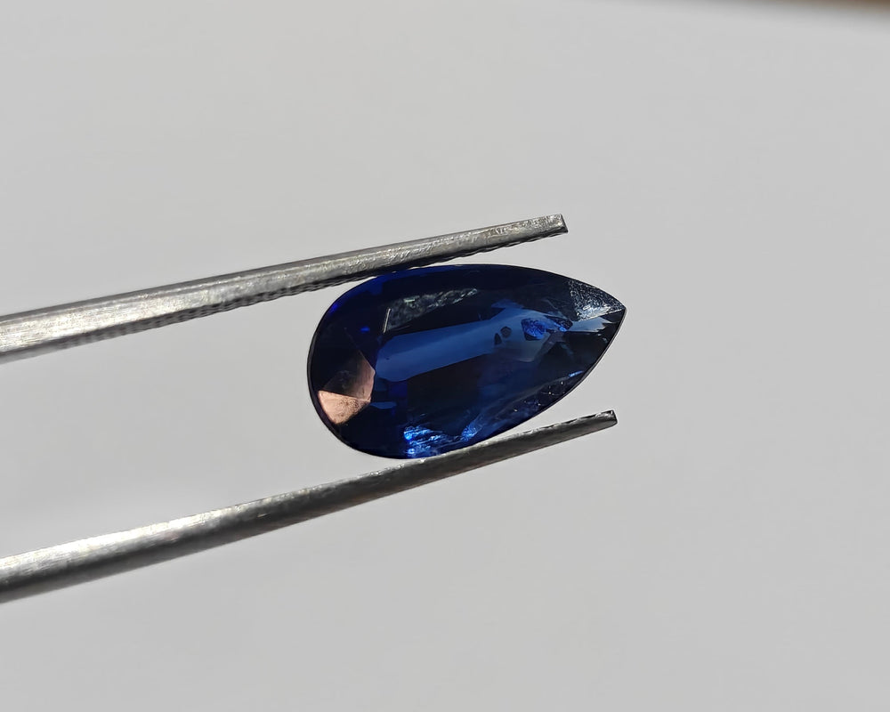 Blue gemstone held by tweezers on a light gray background