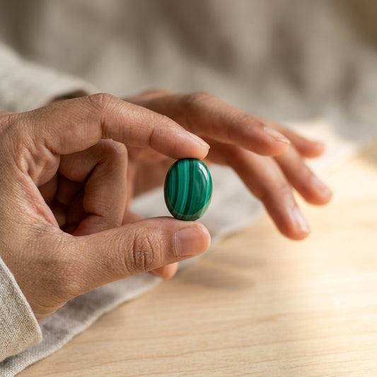 Hand holding a green malachite gemstone on a wooden surface