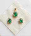 Pair of emerald green teardrop earrings with gold accents on a beige jewelry box.