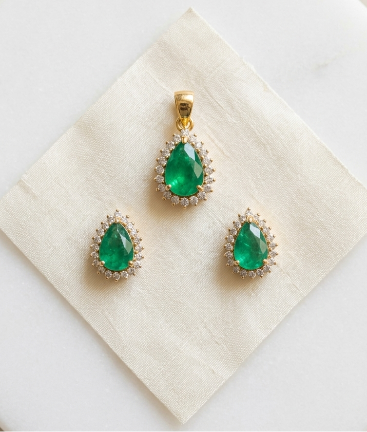 Pair of emerald green teardrop earrings with gold accents on a beige jewelry box.