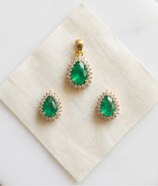 Pair of emerald green teardrop earrings with gold accents on a beige jewelry box.
