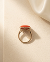 Gold ring with a red moonga stone on a beige surface