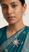 Woman wearing a teal saree with silver jewelry, including earrings and a necklace.
