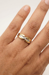 Gold ring with a diamond on a person's finger against a neutral background